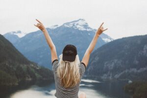 Free blond lady on top of a mountain side with arms in the air loving life.