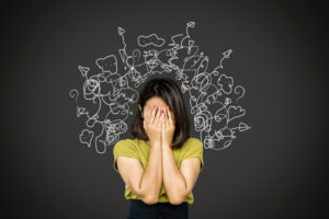 Confused woman with hands covering face. Squiggles and questions marks displayed all around her head showing brain fob and frustration.